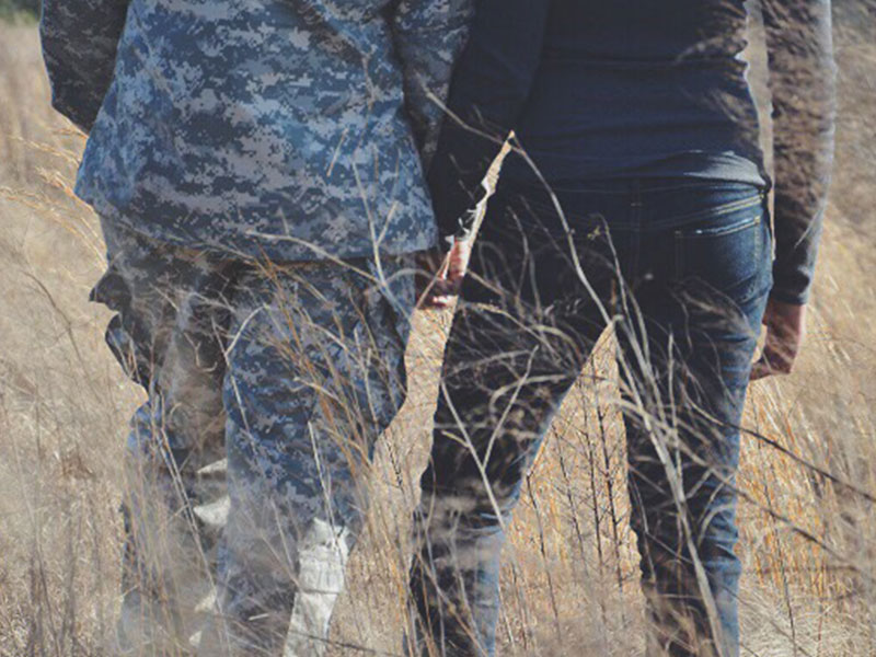 A couple in the armed forces holding hands in a field.