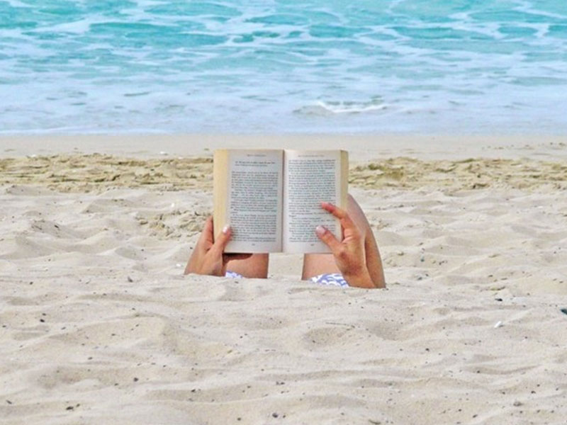 A woman being single and happy as she reads a book on the beach.