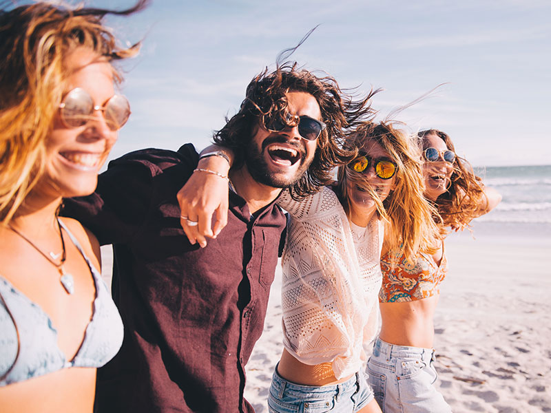 A group of highly successful singles laughing on a beach while they live the single life feeling confident in themselves.