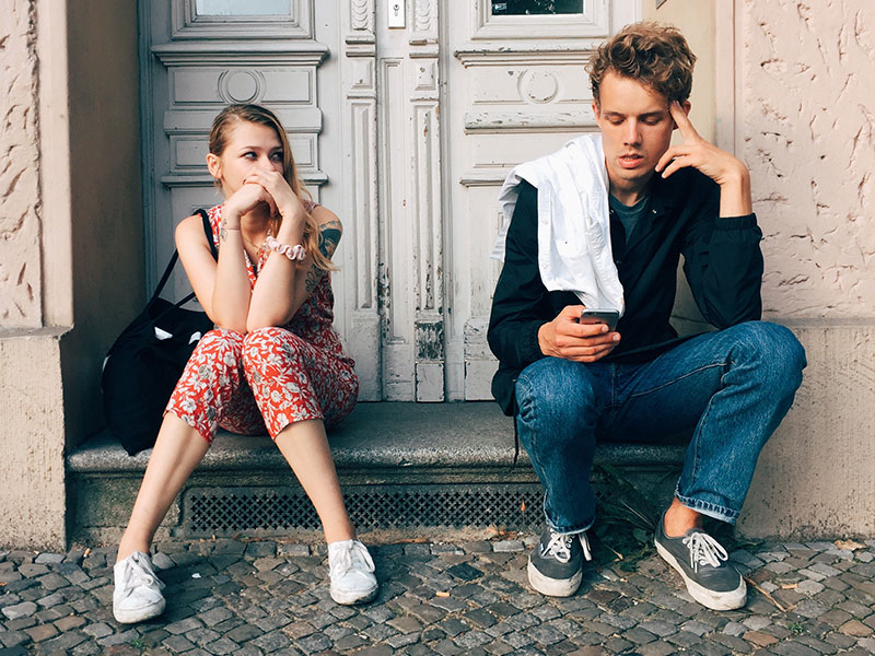 A girl annoyed with her boyfriend while he talks on his phone, thinking these could be signs it's time to break up.