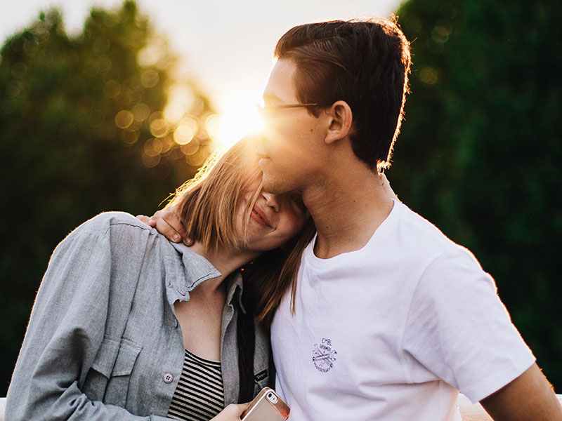 A woman who firgured out what is romance smiling and cuddling with her boyfriend in the sun.
