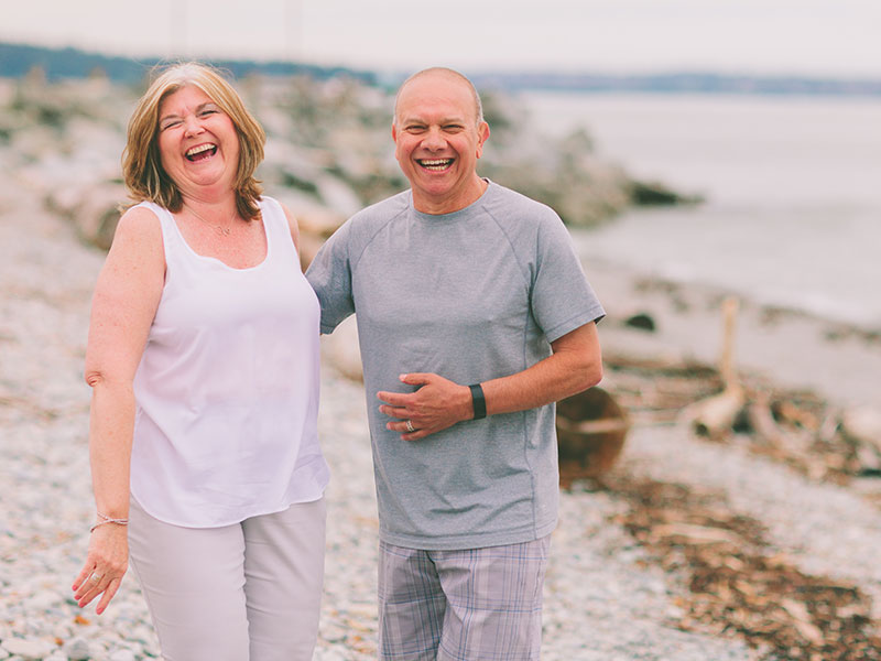 A cute couple dating over 50, laughing and holding hands on the beach.
