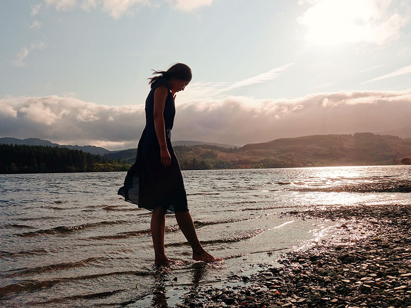 A woman who wants to know how to get over someone you still love walking on the beach and looking down at her feet in the sand.