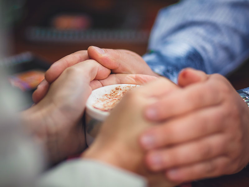 A man who listened to these breaking up tips, holding hands with the woman he's breaking up with over coffee.
