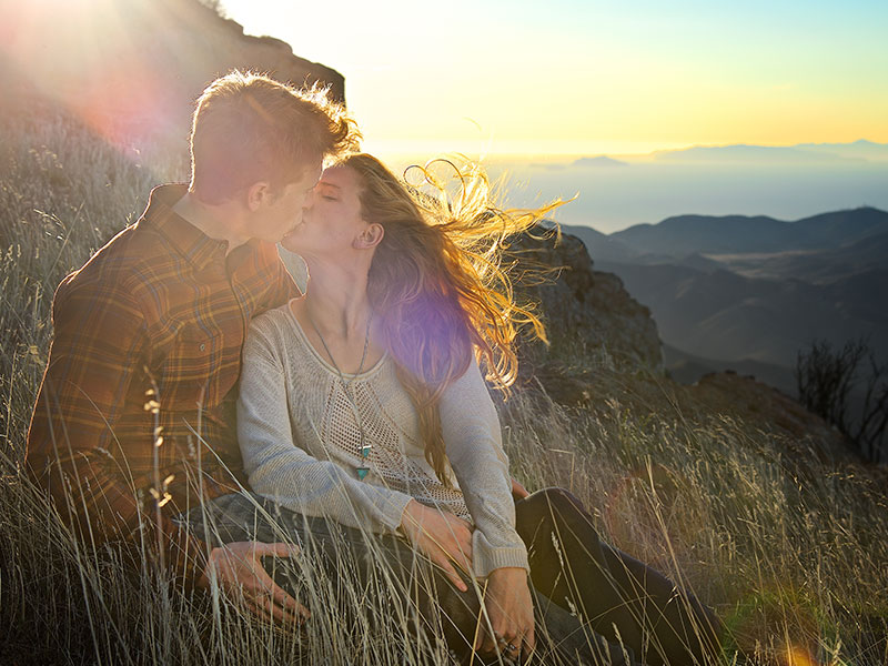 A couple who paid attention to these signs you're in love kissing on top of a mountain at sunset.
