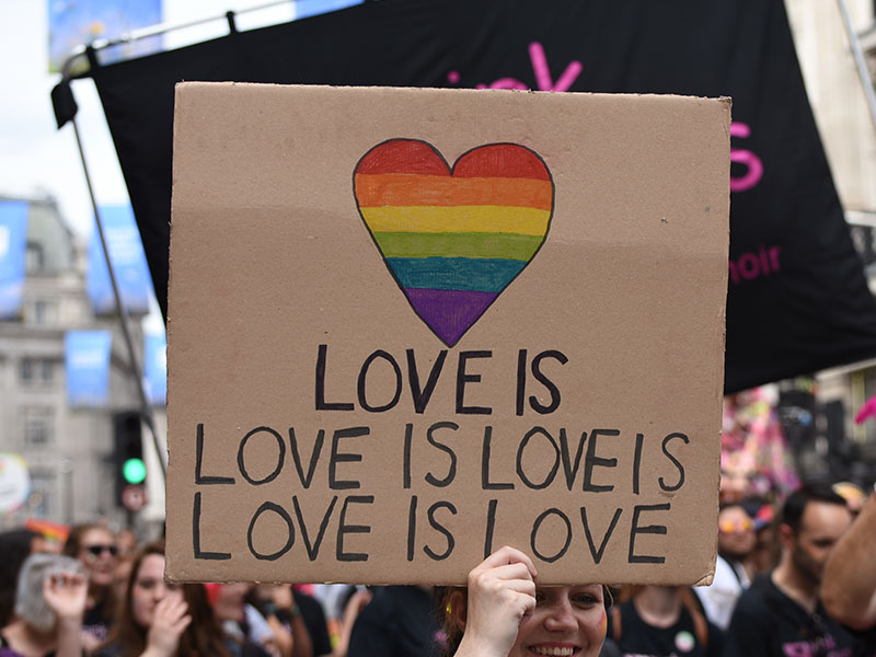 A group of people holding up a sign that says love is love is love is love at a Pride parade.
