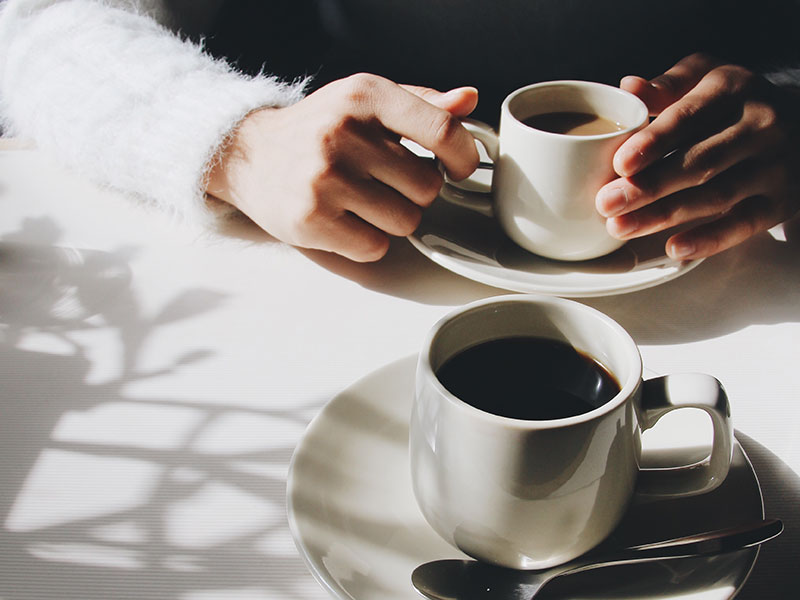 The hands of two people having a "I'm not interested" talk while they hold their coffee cups at a cafe.