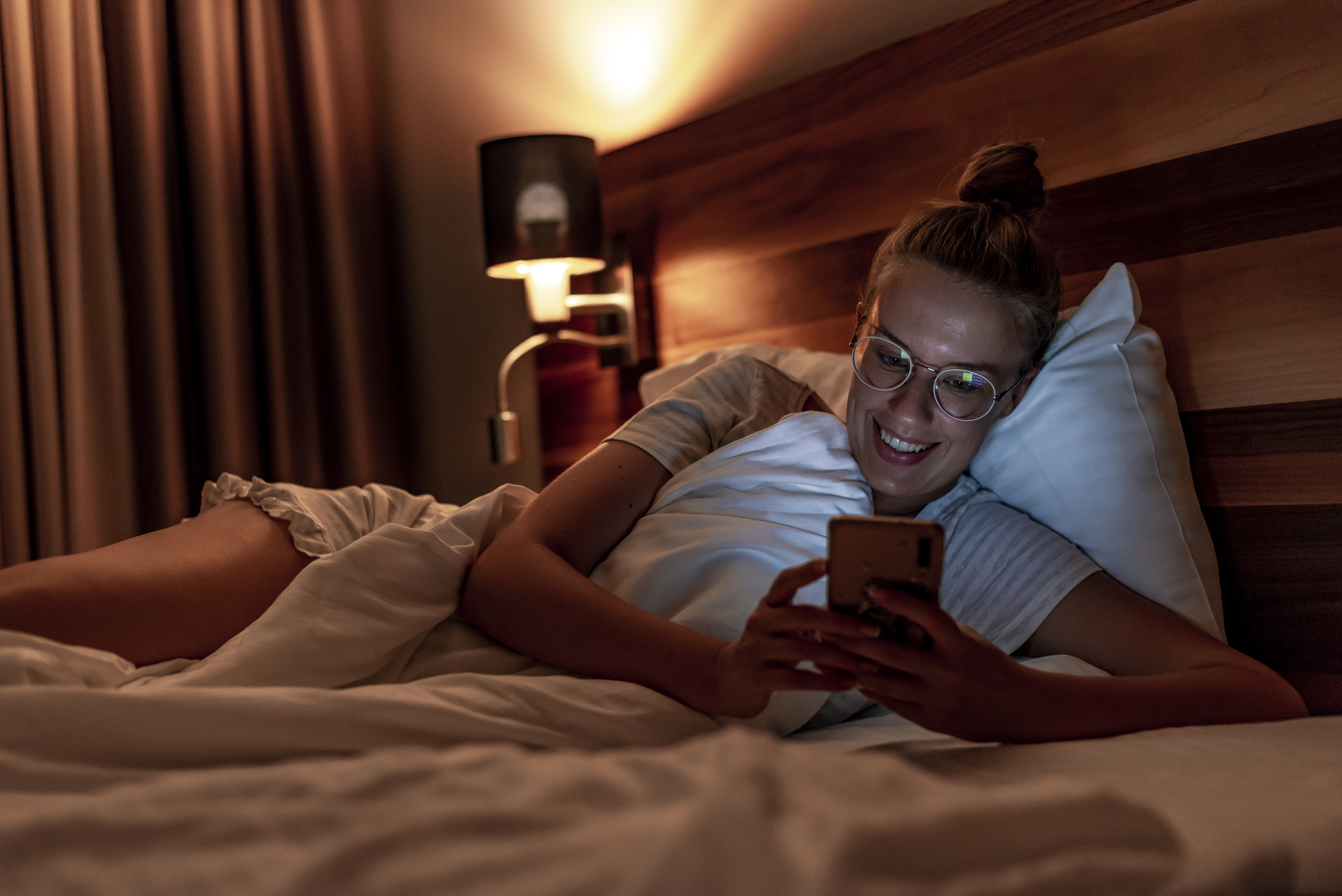 Smiling woman lying in bed and looking at mobile phone after receiving a goodnight love message.