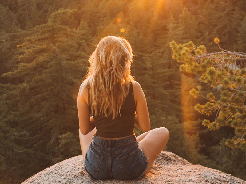 A woman who learned how to build confidence in yourself sitting on a rock in the sun.