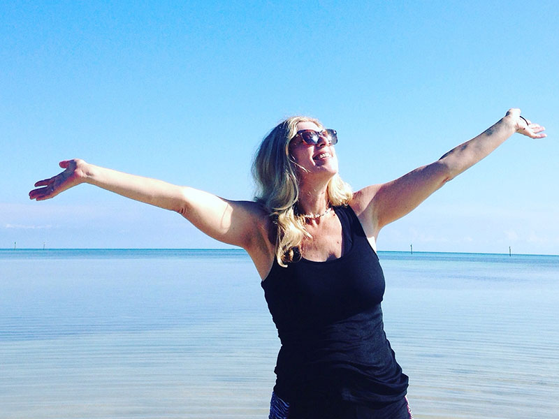 A woman who listened to these breakup tips at the beach with her arms out, embracing life because she’s getting over it.