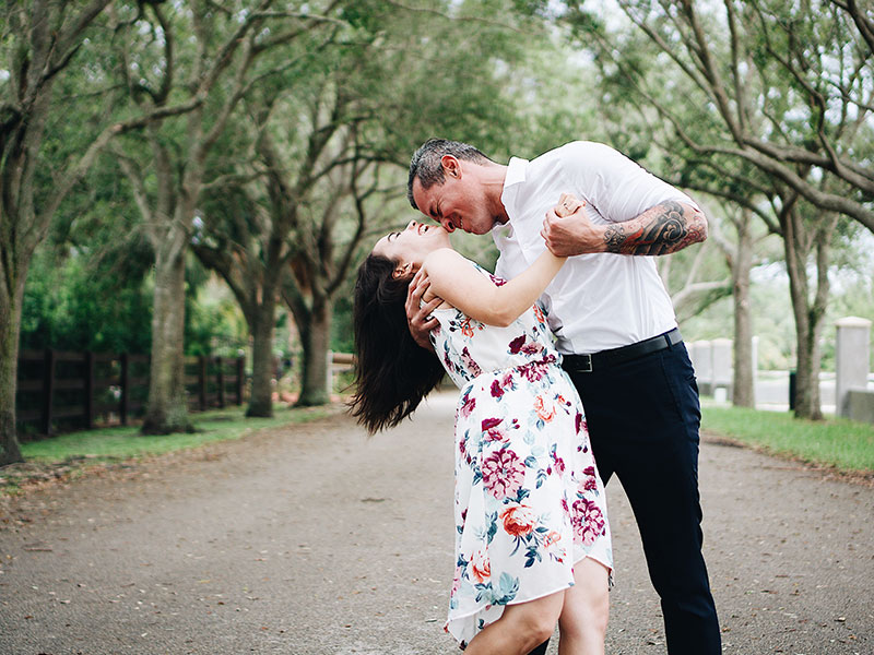 A couple in an older man younger woman relationship dancing under the trees and laughing.