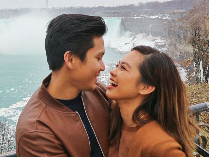 A girl who used these questions to ask a guy you like, laughing with her boyfriend as they take a photo in front of a waterfall.