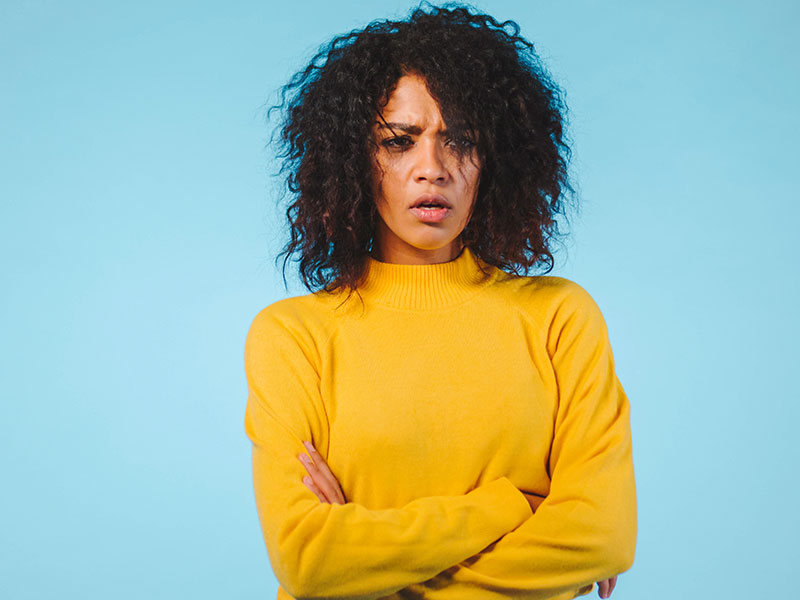 A woman who’s dealing with one of these relationship pet peeves looking annoyed with her arms crossed.