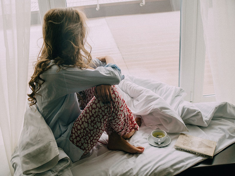 A woman who thinks she may have sarmassophobia, looking out her window and thinking while her coffee sits nearby.