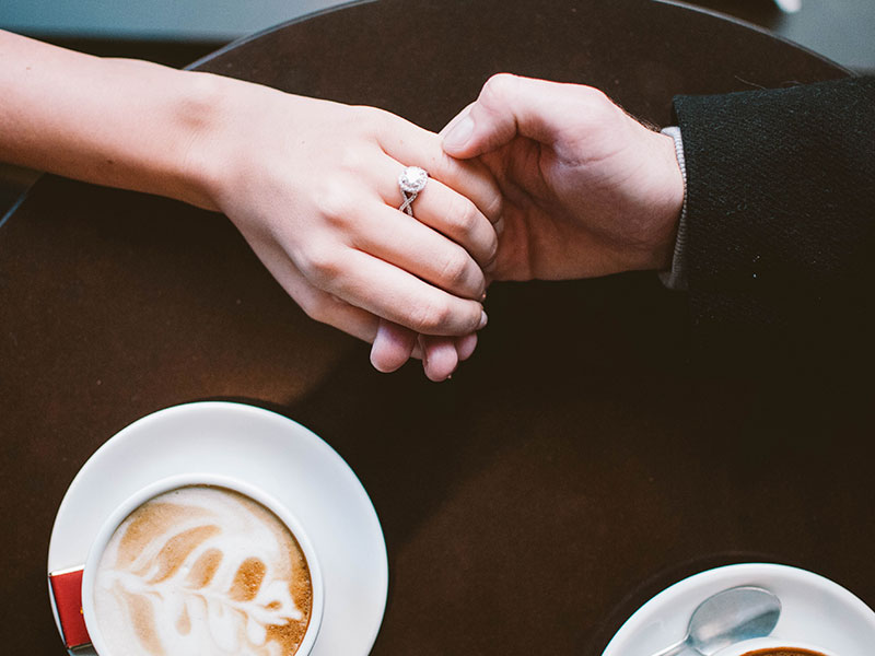 Two friends holding hands across a table, getting into emotional affair territory.