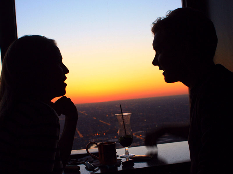 A woman married and flirting with a man as they have a conversation over drinks at sunset.