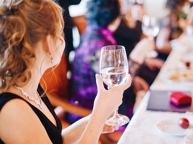 A guest at a wedding holding her glass of water looking around the room for someone to flirt with.