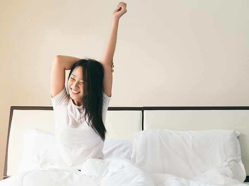 A single girl in bed stretching and smiling in the morning.