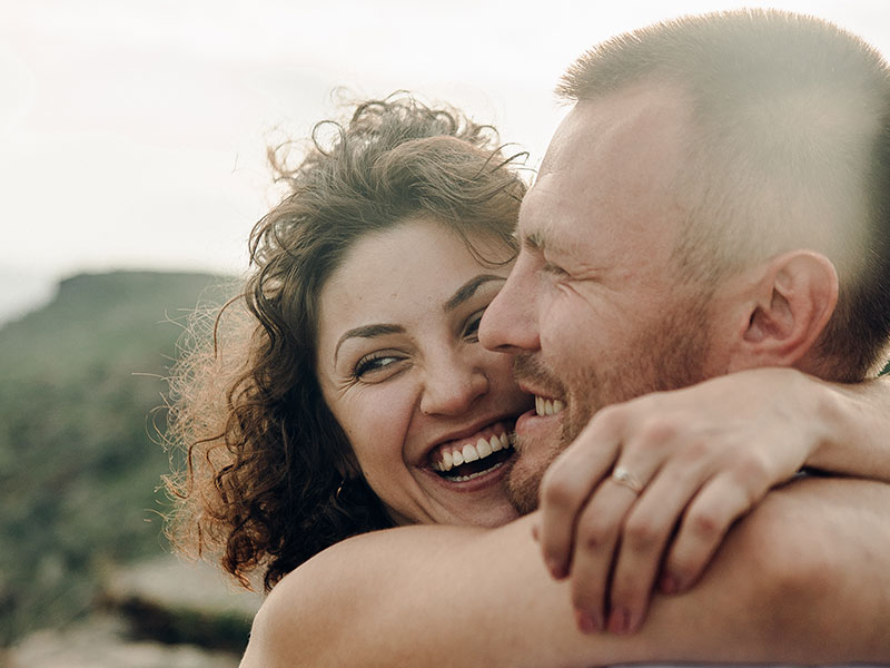 A couple dating in your 40s, smiling and laughing as they hug outside.