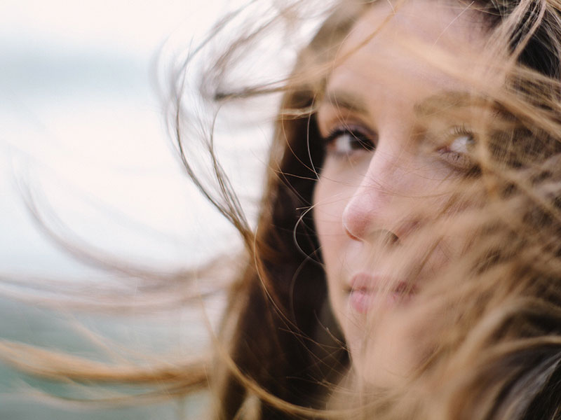 A woman who learned how to forgive a cheater standing in a field while the wind whips her hair around.
