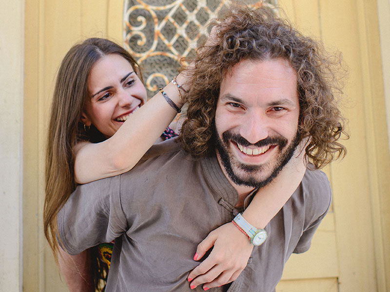 A woman who learned what is flirting, tackling a guy from behind and teasing him as he laughs.