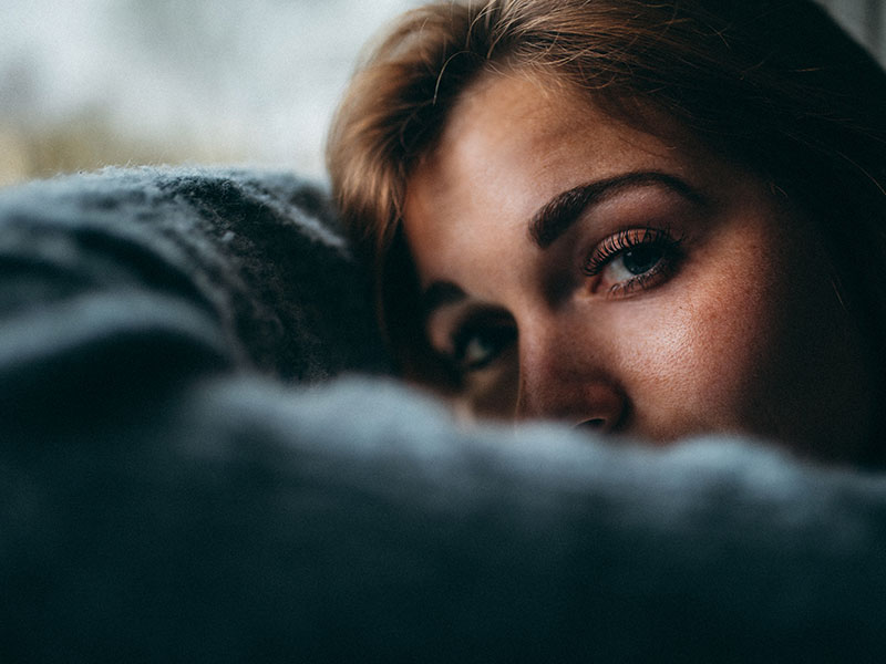 A woman who's in a controlling relationship, looking outside with her head in her arms and thinking.