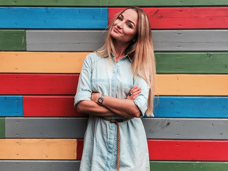 A woman who dresses to impress herself standing confidently in front of a wall in a dress she loves.