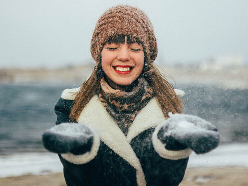 A woman who's learned how to stop attracting players, smiling as she plays in the snow and let's it fall on her.