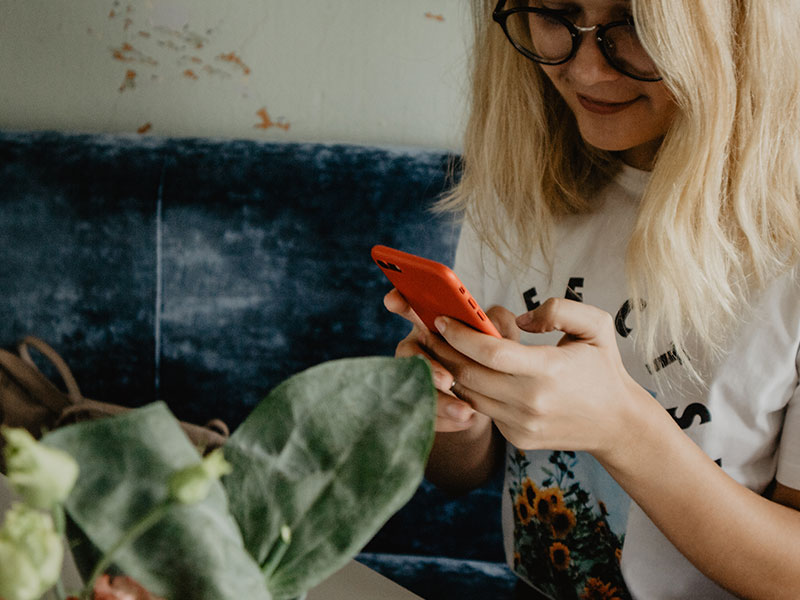 A girl responding to a Tinder first message and laughing on her couch at home.