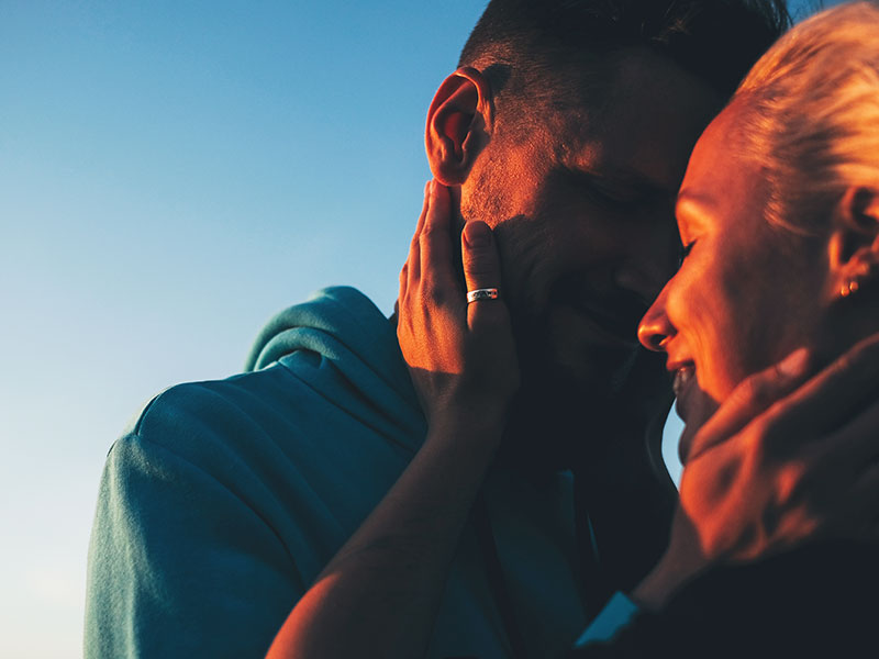 A couple dating over 50, kissing on the beach at sunset.