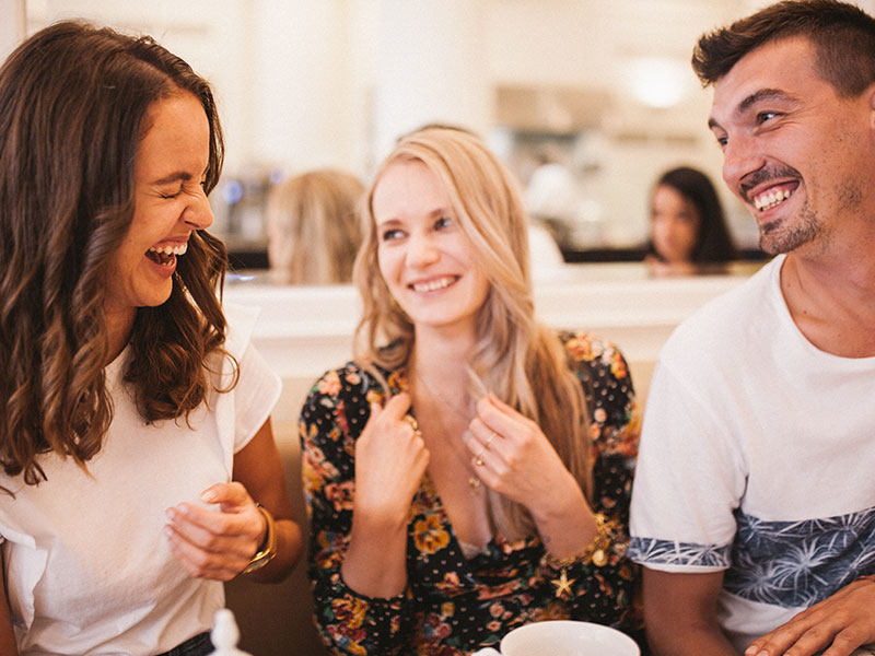 A group of friends laughing together at a table, while one of the woman is dating her friend's ex.