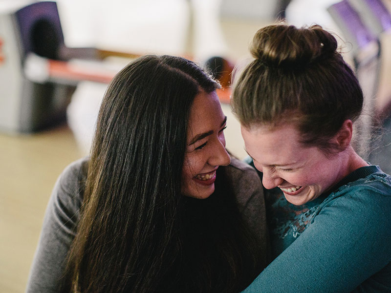 Two women who listened to these lesbian dating tips laughing and flirting while on a date at a bowling alley.