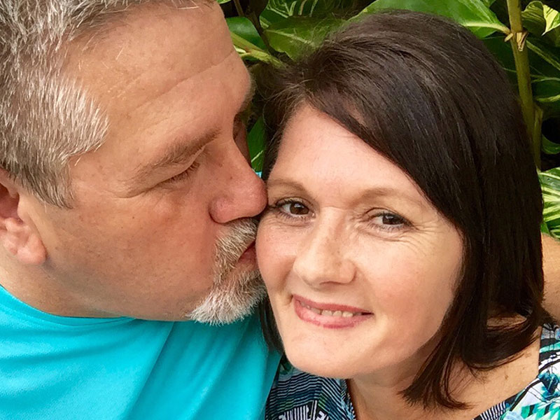 A couple dating after 50 smiling as the man kisses the woman's cheek.