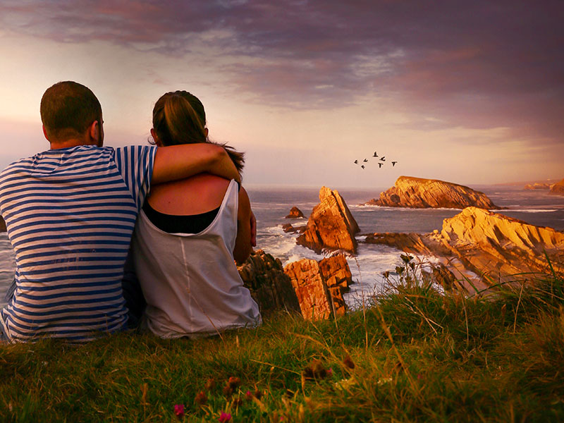 A couple who used on of these first date ideas, sitting on top of a hill looking at the sunset after a hike.