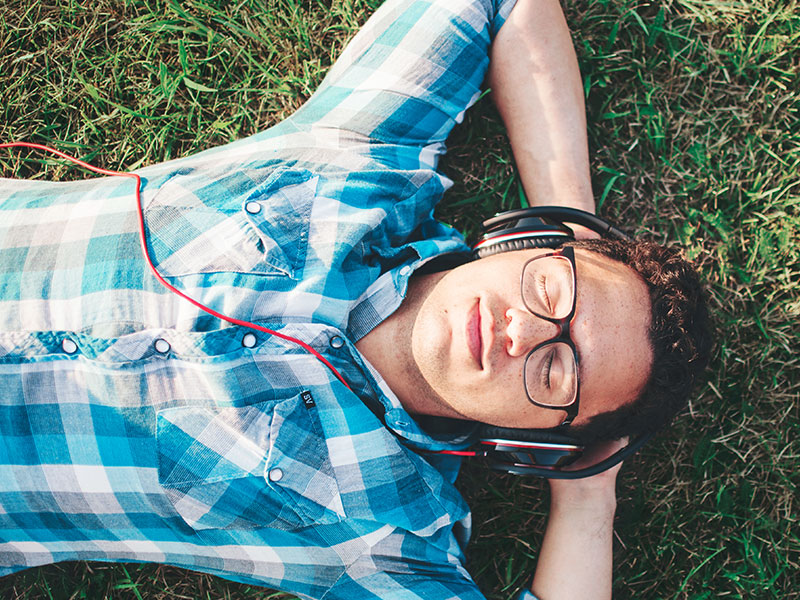 A guy lying in the grass and smiling as he listenings to songs about getting over someone on his headphones.