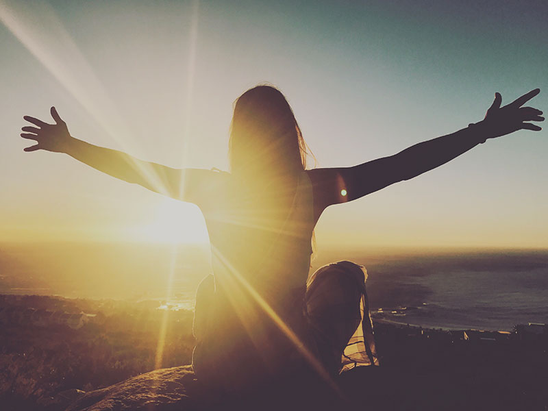 A woman on a mountain embracing the universe and the concept of agape love.
