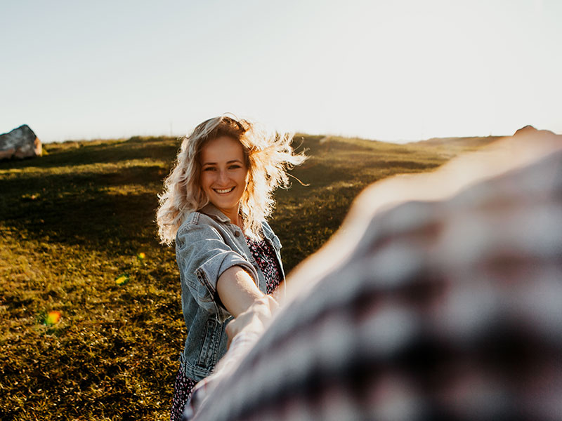 A guy looking at the younger women he's dating as she runs ahead of him through a field.