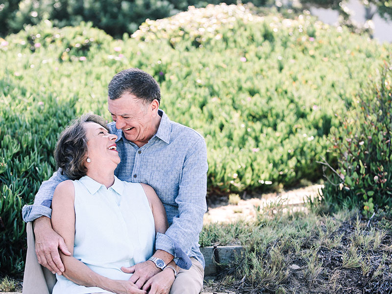 A couple dating over 60 smiling at each other while hugging in a garden.
