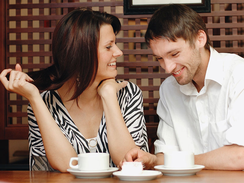 A man who took these flirting tips for guys, talking to a woman at a coffee shop who's laughing at his jokes.
