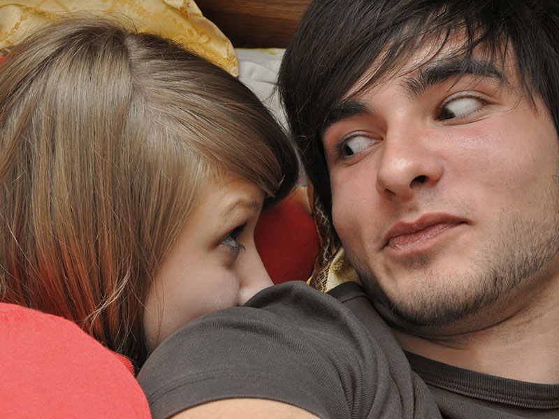 A girl wondering how to make a man want you, looking at the guy she's seeing while in bed.