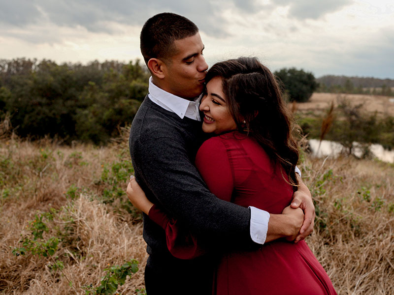 A woman who's dating a man, hugghing him and laughing outside in the wind.