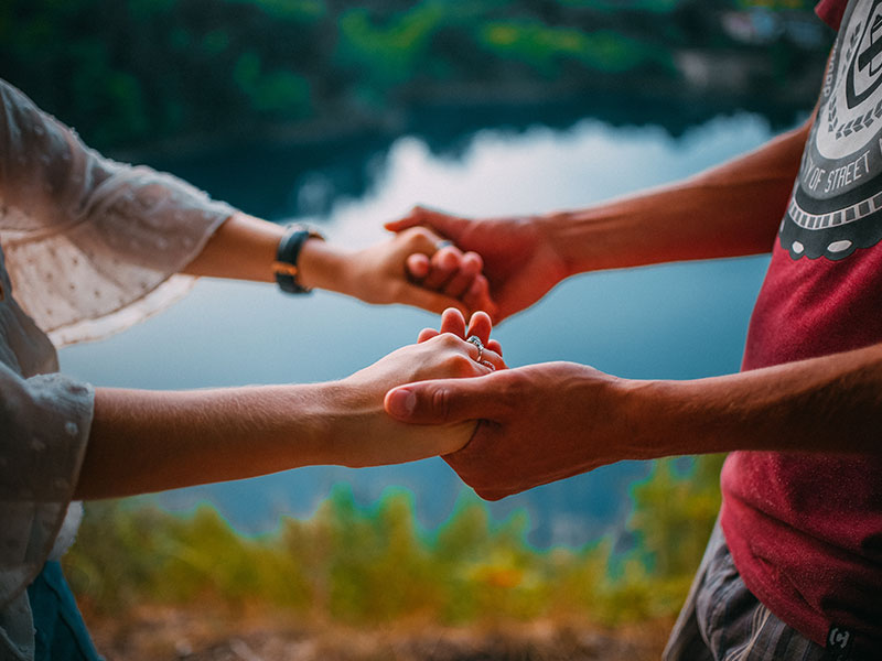 A woman who's wondering, "Why do you love me?" holding hands by a lake with her partner who's telling her just that.