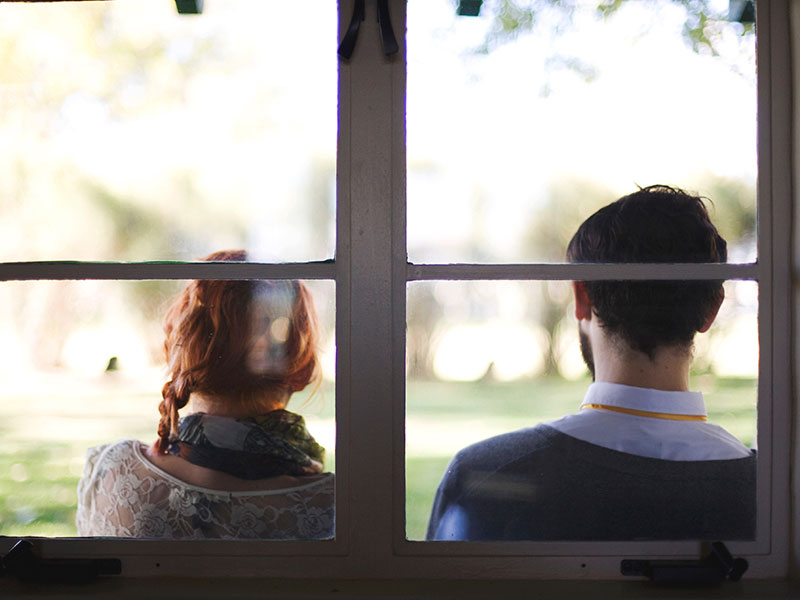 A man who has a fear of commitment sitting outside leaning against a window with her girlfriend as they have a discussion.