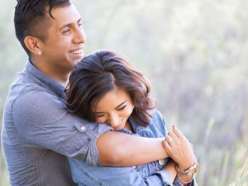 A man who is a jealous boyfriend hugging his girlfriend tight as they laugh together.