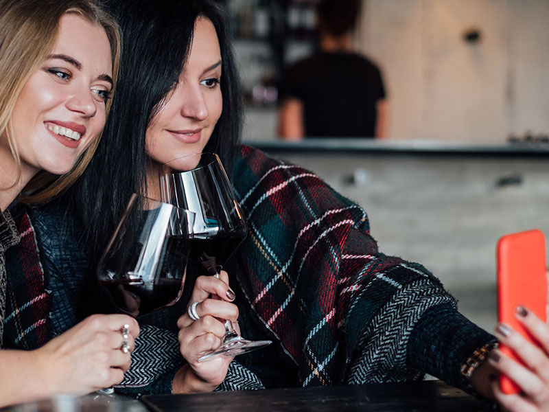 Two women who are bad friends smiling and taking a selfie together with wine.