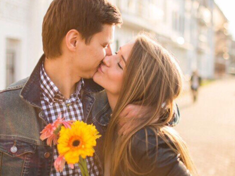 A guy who learned how to woo someone, kissing his girlfriend while holding flowers.