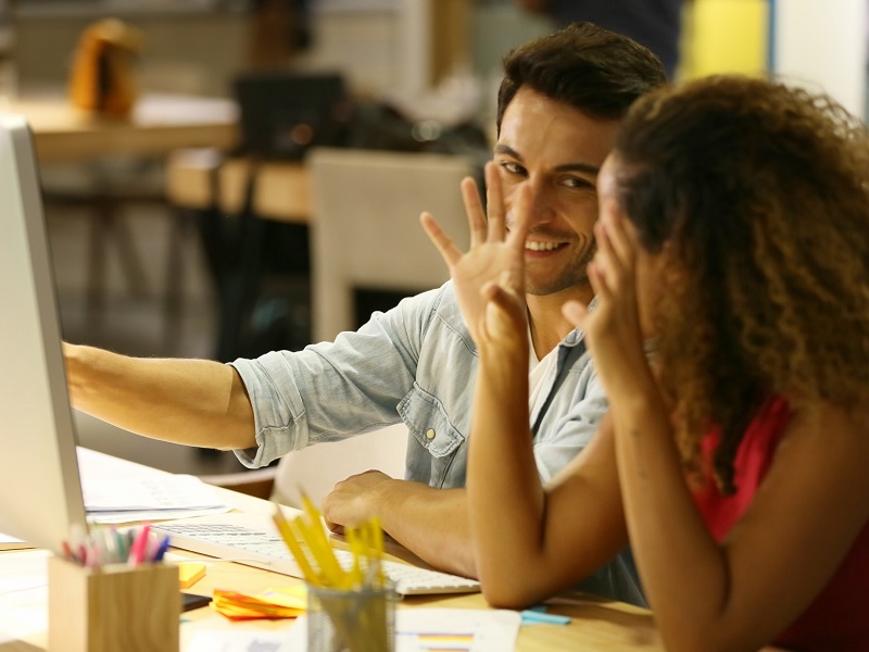 couple laughing at computer guessing how to tell if a guy at work likes you