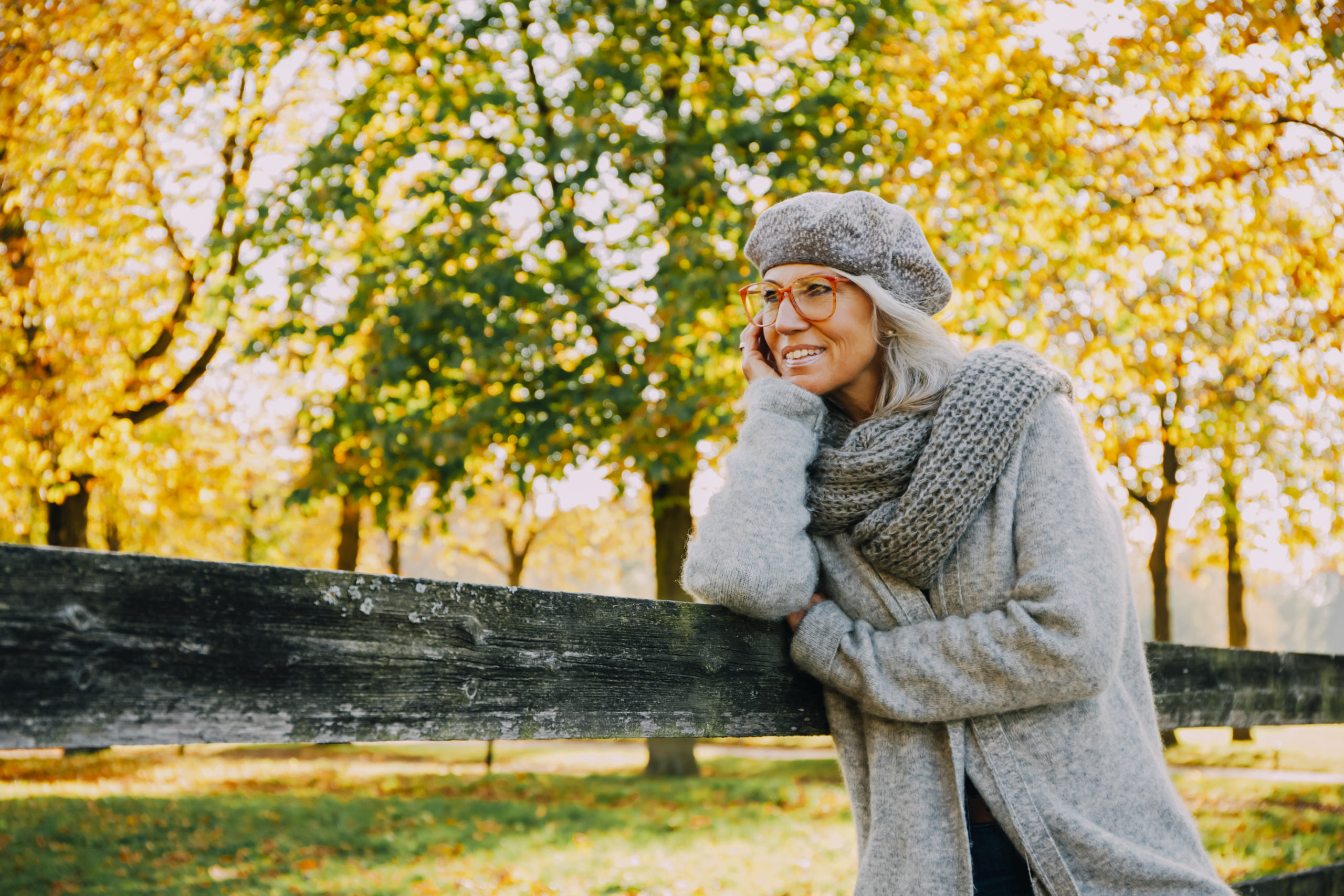 attractive senior, single woman leaning on fence smiling in Autumn