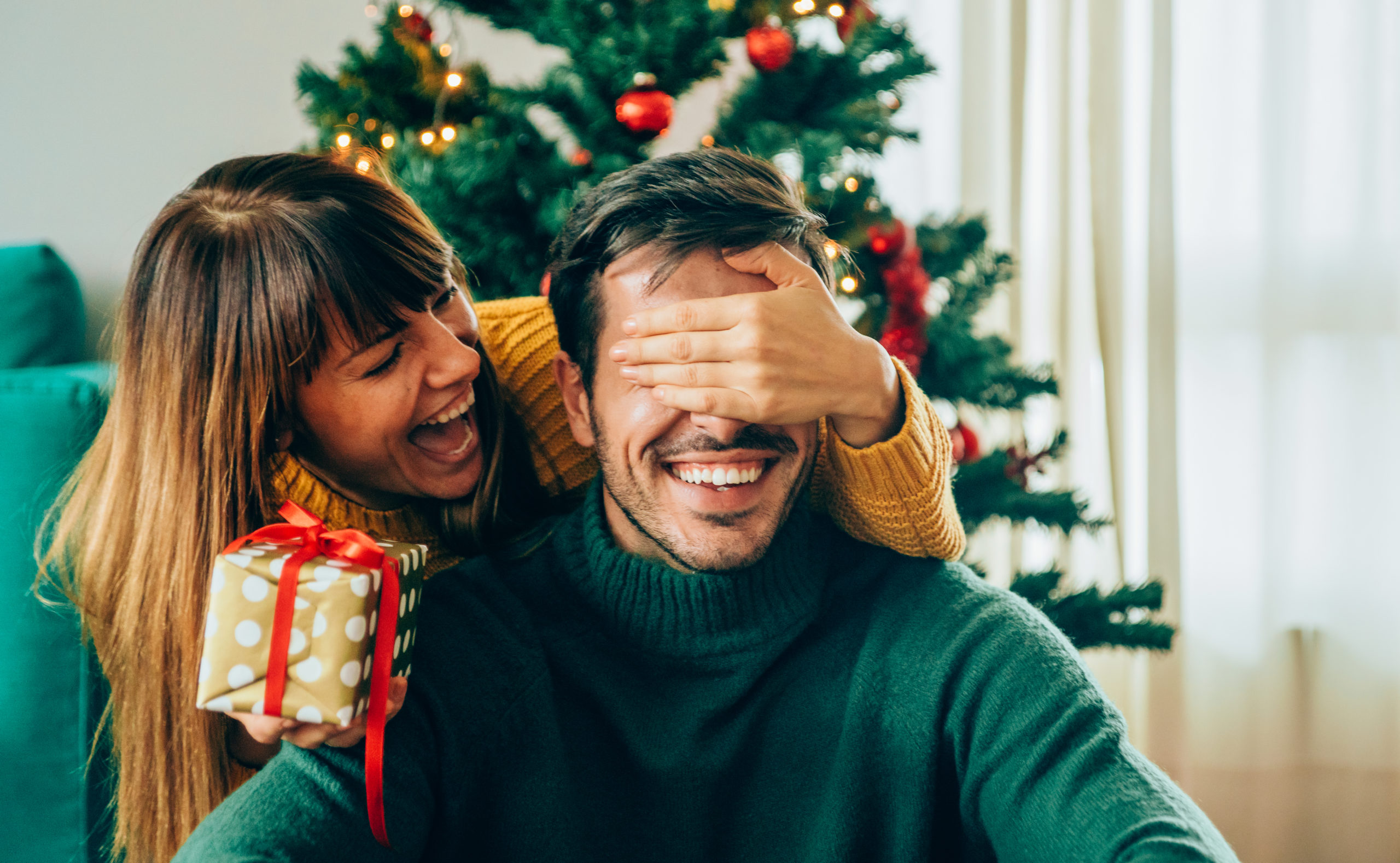 Happy couple smiling and laughing together while exchanging their cute Christmas gift ideas.