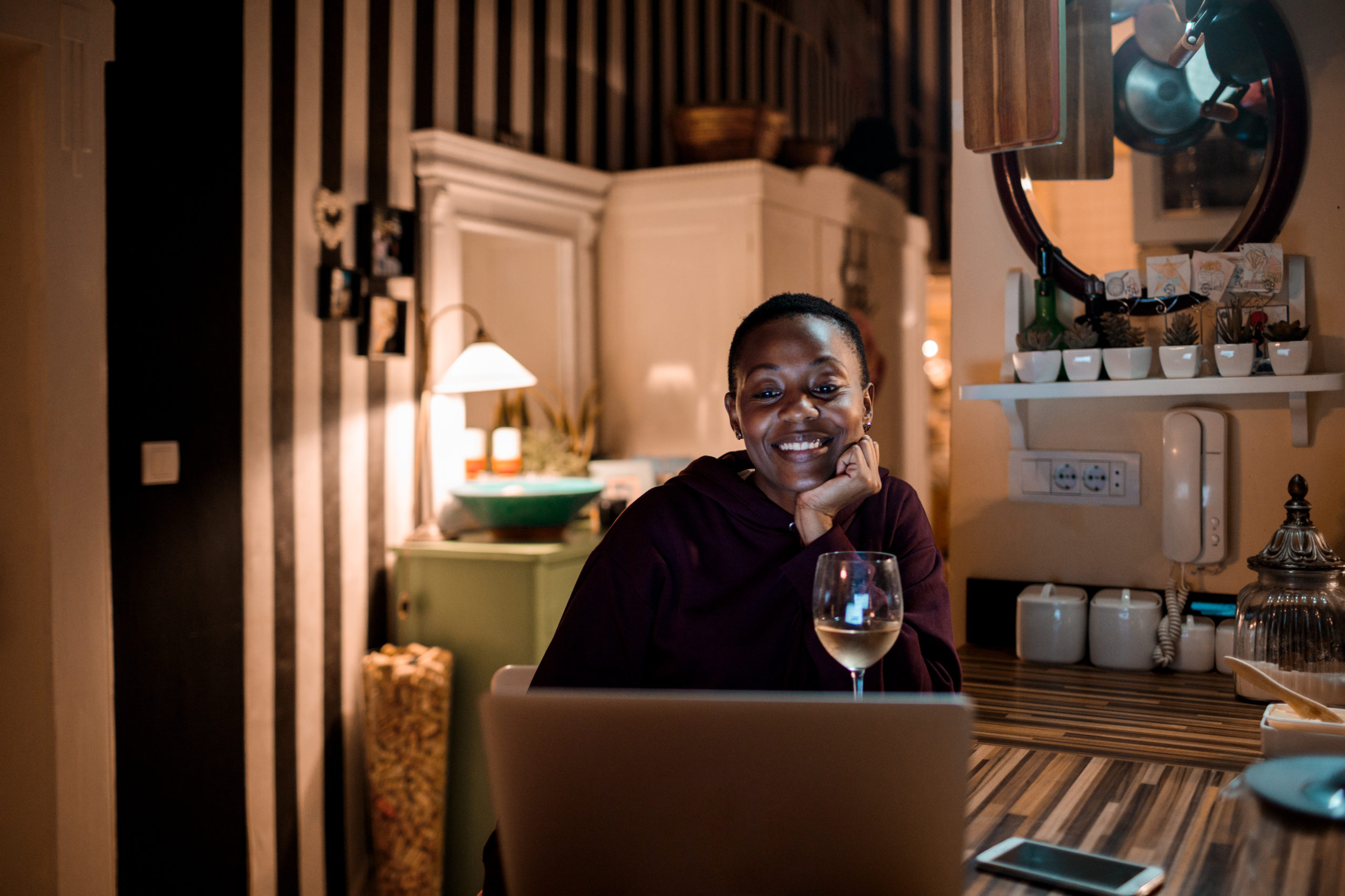 Young woman sitting at table using her laptop and smiling while trying out a fun Zoom date idea.